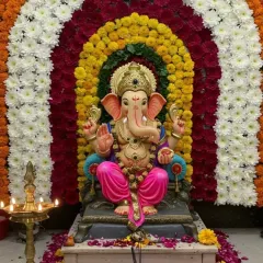 For Ganpati festival celebrations, I create stunning backdrops like this one. This mandap decoration features a dense arch made entirely of fresh flowers, including white chrysanthemums, yellow and orange marigolds, and red carnations, for a vibrant and traditional look.