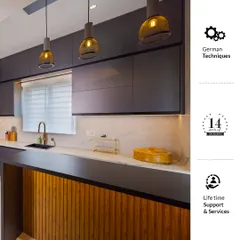 This modern kitchen showcases our commitment to quality, combining German techniques for durability with lifetime support and service. The design features dark grey cabinets, a wood-paneled breakfast bar, and stylish pendant lights.
