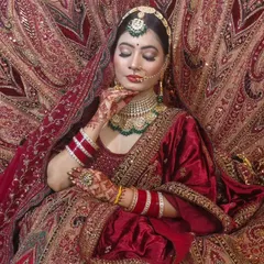 A truly royal look featuring a rich red velvet lehenga with detailed gold embroidery. The matching jewellery set with green accents completes this traditional bridal ensemble.