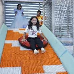 The doughnut slide offers a unique sliding experience. Here, a girl glides down on an inflatable tube, with our staff member watching closely from the top.