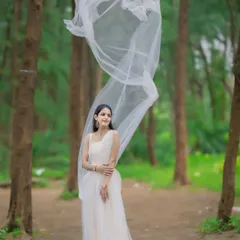 This ethereal white gown with its flowing net trail is perfect for a romantic shoot in nature. The lightweight fabric creates a beautiful, airy effect among the trees.