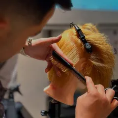 A close-up shot of a student executing a precise cut. Notice the focus on comb tension and finger angle, which are critical details for creating structured and balanced haircuts.