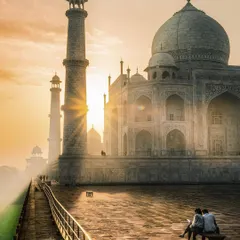 A romantic view of the Taj Mahal at sunrise, with a couple sitting on a bench in the foreground, perfectly blending iconic architecture with a human story.
