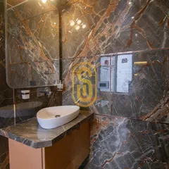 Another view of the dark marble bathroom, focusing on the vanity area. The uniquely shaped mirror and countertop sink add a touch of artistic flair to the functional space.