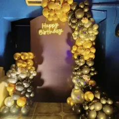 This stylish birthday decoration uses a black and gold balloon arch to create a bold statement. The "Happy Birthday" neon sign adds a modern touch, perfect for an evening celebration.