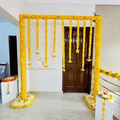 A classic and vibrant Haldi ceremony backdrop. This simple yet elegant design features a frame fully covered in bright yellow marigolds with hanging floral strings, perfect for home-based pre-wedding functions.