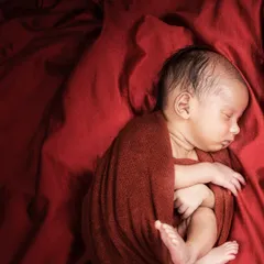 A dramatic and moody portrait using a deep red wrap and background. This style creates a rich, artistic feel, focusing on the baby's curled-up form.
