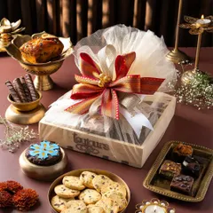 A beautifully wrapped wooden gift box, tied with a traditional red and gold ribbon, surrounded by a selection of my Diwali treats like cookies, brownies, and a mini cake. This highlights my elegant packaging and the delicious items that can be included.