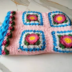 A folded view of the Lydia blanket, highlighting the texture of the stitches and the puffy rosebud border.