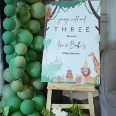 A personalized welcome sign on an easel, framed by a cascade of green balloons, greeted guests for Ira and Bodhi's "Young, Wild and Three" birthday celebration. It's a small touch that makes a big first impression.