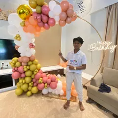 One of our decorators posing with the completed organic balloon arch. This warm-toned setup with a personalized bubble balloon and neon sign was a joy to create.