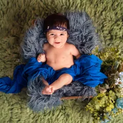 A beautiful color combination of royal blue and green makes this baby portrait pop. The baby is propped up in a basket, looking off to the side with a curious expression.