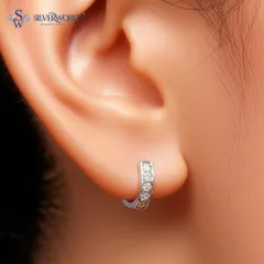 A close-up of our zirconia huggie earrings, worn on the ear. These small hoops sit snugly and are lined with sparkling stones, perfect for a minimalist yet glamorous look.