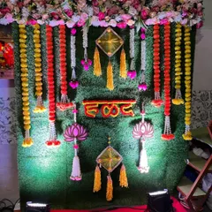 A traditional Haldi backdrop made of a lush green wall. It's decorated with marigold and rose flower strings, along with decorative hangings.