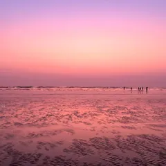 A beautiful photograph of a Mumbai beach at sunset, with the wet sand reflecting the soft pink and purple hues of the sky.