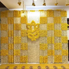 This haldi backdrop was created in the client's living room. I designed a checkerboard pattern using yellow and white flower strings and placed a Ganesha motif made of marigolds in the center for a traditional touch.