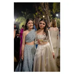 Sisters styled by us for a sangeet night. One wears a chic one-shoulder lehenga in dusty blue, while the other is in a classic ivory lehenga, showcasing how individual styles can still look cohesive.