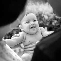 Sometimes, the most powerful images are the quiet ones. This black and white portrait, framed by the parents, focuses purely on the baby's happy expression and the incredible bond they share.