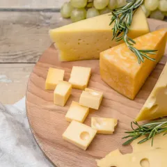 A rustic wooden board with wedges of Swiss and cheddar cheese, garnished with fresh rosemary. This simple yet elegant presentation highlights the quality of the ingredients.