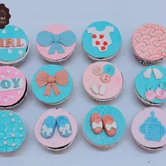 A set of adorable baby shower cupcakes. Each cupcake has a unique, hand-crafted fondant topper, including baby clothes, bows, bottles, and tiny feet.