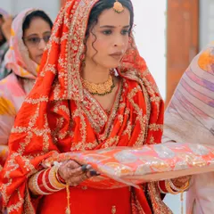 A candid moment during the ceremony. The intricate embroidery on her red dupatta and her elegant gold jewelry are highlighted beautifully in this shot.