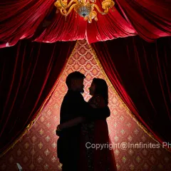 A silhouette captured against a rich, theatrical red curtain backdrop. This technique creates a sense of intimacy and drama, focusing entirely on the couple's embrace.