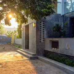 The entrance at sunset, with integrated lighting highlighting the different textures of the facade, from the smooth concrete to the rough stone and perforated brickwork.