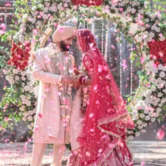 A magical moment as a Sikh couple shares their first look under a stunning floral arch, with a cascade of pink petals showering down around them. This image perfectly captures the joy and emotion of the Varmala ceremony.