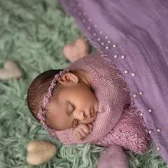 This top-down view shows a baby swaddled in a beautiful lavender wrap, surrounded by soft felt hearts. The contrast of the purple wrap against the mint green fur creates a lovely color palette.