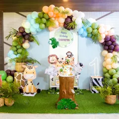 A stunning jungle safari themed backdrop for a first birthday, featuring cute cartoon animals, a tree stump cake stand, and a lush balloon arch.