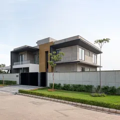 A photograph of the completed Jindal Residence in Sonipat. This view shows the home's strong, modern form set within a carefully manicured landscape, creating a private and tranquil environment.