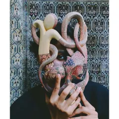 A striking image from 'Roots' where the model's face is partially obscured by an ornate, hand-painted mask. This styling choice explores the idea of identity as both a shield and a form of expression.