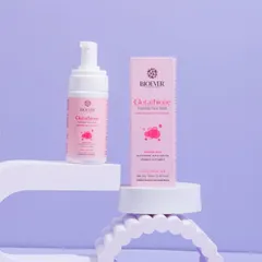 A creative product shot of a foaming face wash, using abstract props and a pastel color palette. This modern and clean aesthetic is ideal for a skincare brand's launch campaign.