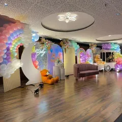 A side view of the entire pastel rainbow stage, showing how all the elements come together. The design includes a large balloon rainbow, a crescent moon prop, multiple backdrops, and a cute candy cart.