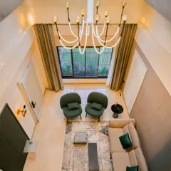 This high-angle view of a Guwahati residence captures the full scope of a cohesive lighting plan. The modern chandelier draws the eye, while subtle wall and accent lights create a warm, layered glow throughout the double-height living space.