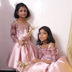 Picture-perfect elegance for two. These matching sister dresses in dusty rose satin feature exquisite off-the-shoulder lace sleeves and a full pleated skirt, designed for the most memorable occasions.
