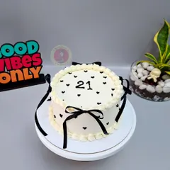 A chic vintage-style cake for a 21st birthday, decorated with delicate black hearts and elegant black ribbons.