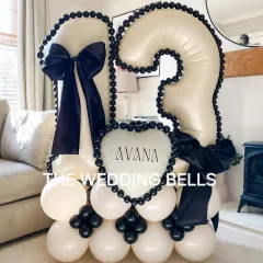 A chic and modern balloon bouquet for a 13th birthday. The black and white color scheme with large satin bows gives it a sophisticated look, and the personalized 'Avana' heart balloon makes it a unique centerpiece for the celebration.