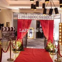 A red carpet 'Premiere Night' entrance for a Bollywood-themed 90th birthday party. The setup includes velvet ropes, a custom clapperboard, and movie poster displays.