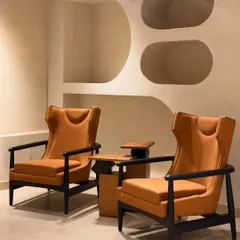 A pair of our custom wingback chairs in a striking tan leatherette, set against a neutral backdrop. The high back and dark wood frame create a sophisticated silhouette, ideal for a modern lounge or study.