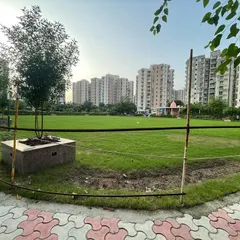 A wide view of a newly landscaped park in a residential society. The project included laying a large, healthy lawn and planting young trees in designated planters along the perimeter.