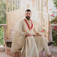 A portrait of a royal groom at Lohagarh Fort Resort. His cream-colored sherwani and red beaded necklace perfectly complement the heritage aesthetic of the venue.