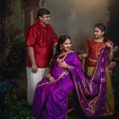 A family portrait featuring an expecting mother in a purple saree, her husband, and their daughter. The daughter helps hold the saree's pallu, adding a sweet, interactive element to this traditional shoot.