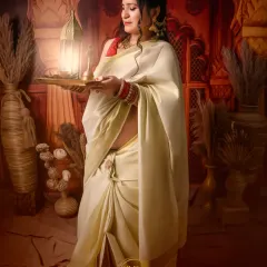 A serene and spiritual-themed maternity portrait. The mother-to-be, dressed in a traditional white saree, holds a lit diya, creating a peaceful and culturally significant image.