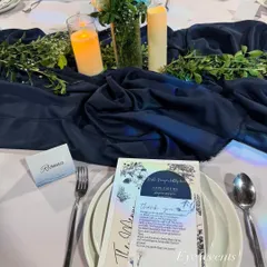 A personalized place setting from a blue and white themed event. The custom menu and name card feature elegant typography and design elements that complement the overall decor, making each guest feel special.