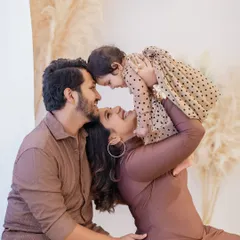 The pure joy of a first birthday. A mother in a beautiful brown dress lifts her smiling baby girl, dressed in a polka-dot frock, high in the air. This candid moment from a family birthday photoshoot is full of laughter and love.