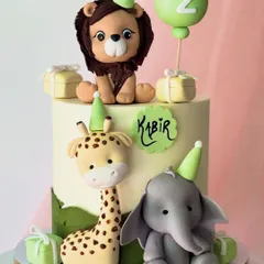 A cheerful safari party cake for Kabir's second birthday. This design includes fondant figures of a lion, giraffe, and elephant wearing party hats, ready to celebrate.