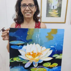An adult student beams with pride, holding her beautiful acrylic painting of a water lily. It's never too late to pick up a brush and discover a new passion or revisit an old hobby.