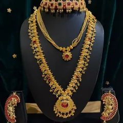 This rental set features a stunning choker and a long haar with peacock-shaped earrings, all studded with red and green stones.