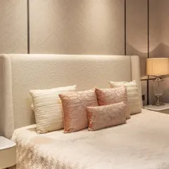 A detailed shot of the custom-upholstered headboard and a curated selection of pillows. Every element is chosen to contribute to a feeling of softness and personal comfort.